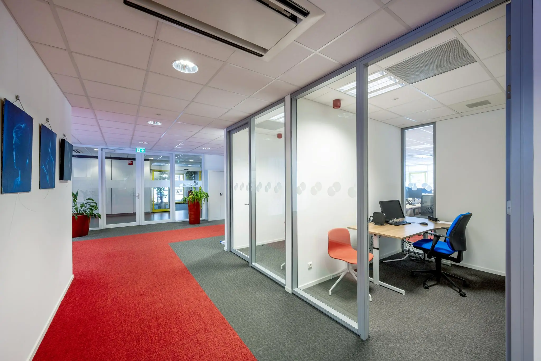 Moderne kantoorruimte aan de Jan Tooropstraat met glazen vergaderruimtes en kleurrijk tapijt.